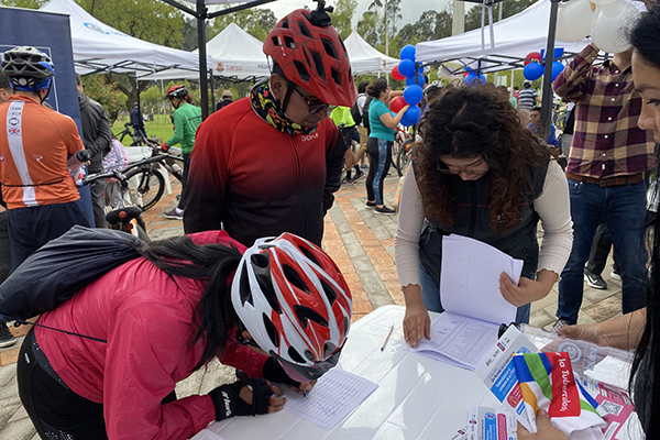 Woman and man with bicycle helmets on looking at a stand with informative material and people helping them